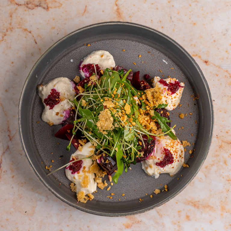 An Auri dish with greens and colourful toppings on a dark plate